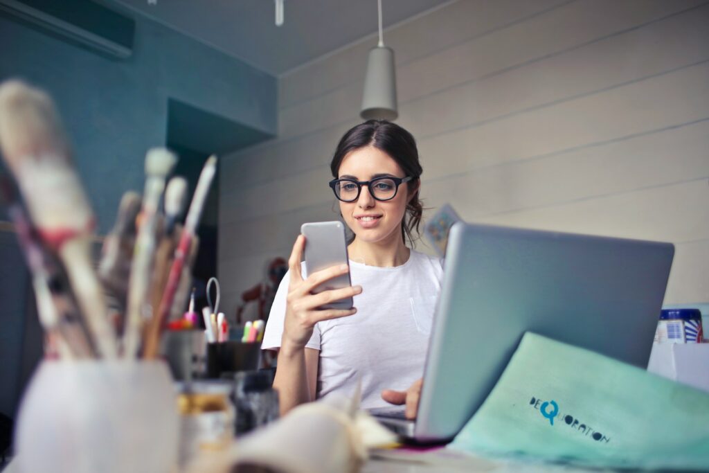 Woman wearing glasses using smartphone at desk. The desk artists materials.